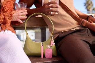 Person holding a pink 30ml perfume bottle with a green handbag in the foreground.