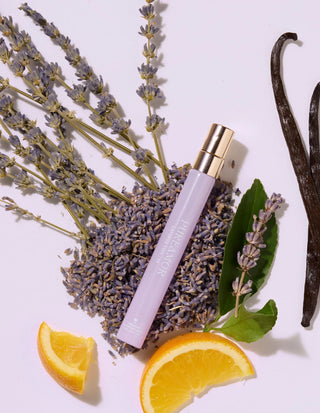 travel spray with lavender, vanilla beans, and orange slices on a white background