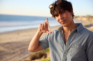 Young man holding a 12ml travel spray of pheromone perfume by the beach, showcasing the scent in a natural, sunlit setting.