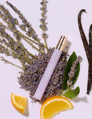 travel spray with lavender, vanilla beans, and orange slices on a white background