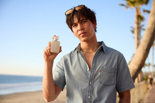 Man holding a 30ml bottle of perfume on a beach with palm trees in the background